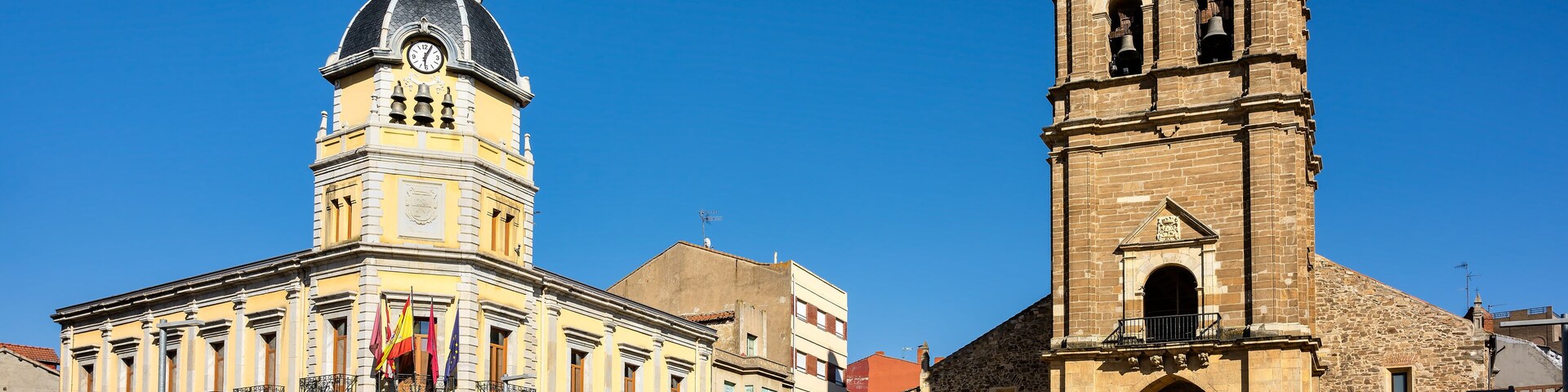 Cityscape of old town La Bañeza in Castile and Leon, Spain, with historic town hall building and landmark Saint Mary church on the main town square.