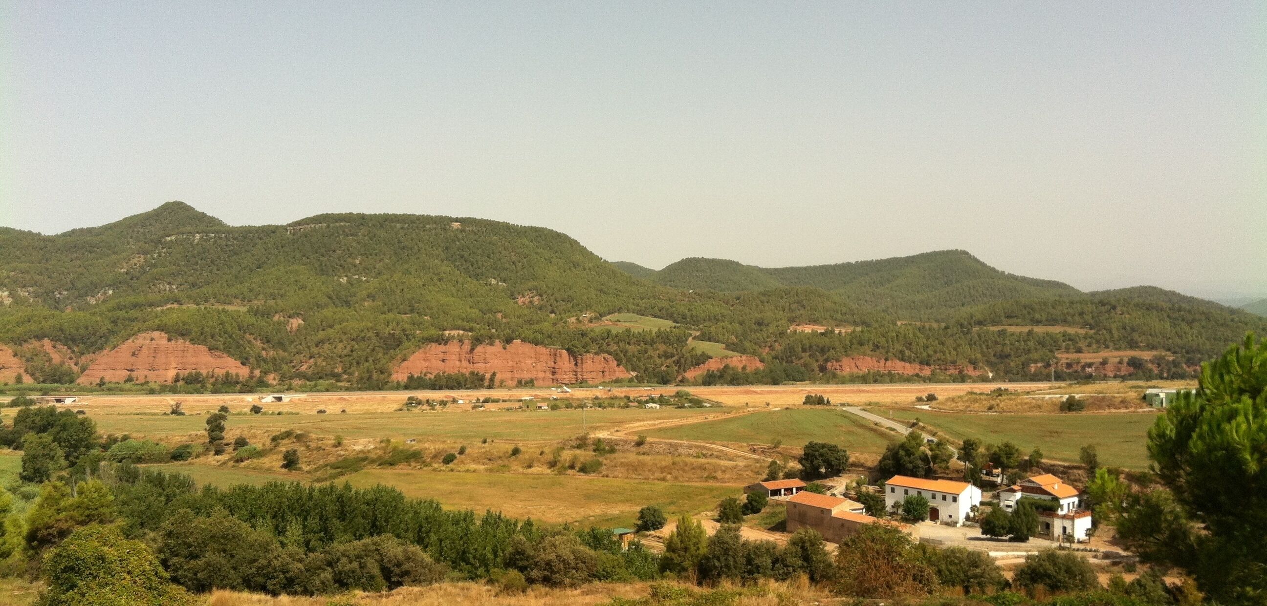 A rural landscape with rolling hills, a small village, and red rock formations.