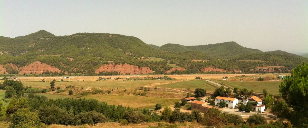 A rural landscape with rolling hills, a small village, and red rock formations.