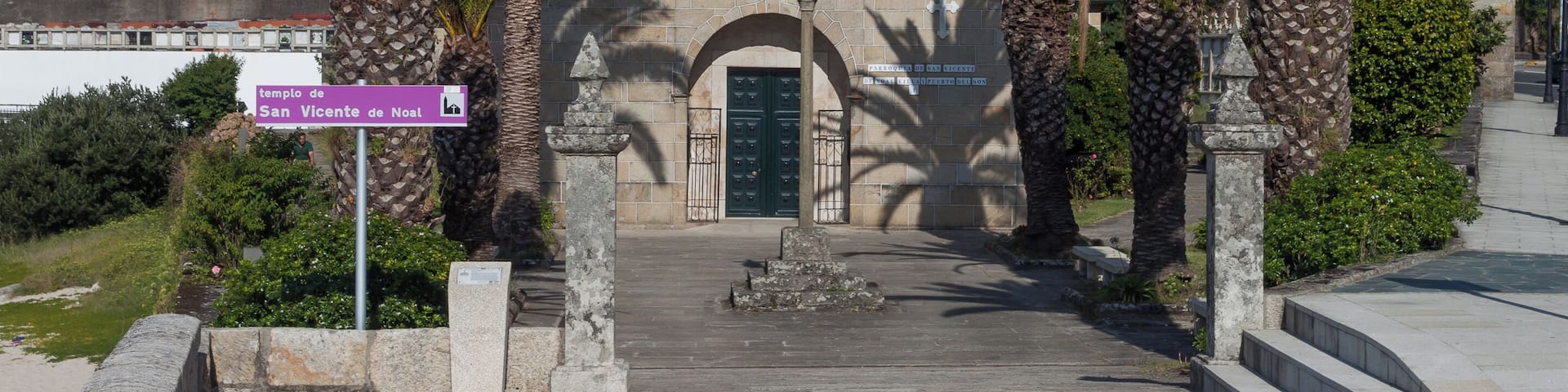 A church with a bell tower, palm trees, and a sign reading "templo de San Vicente de Noel".
