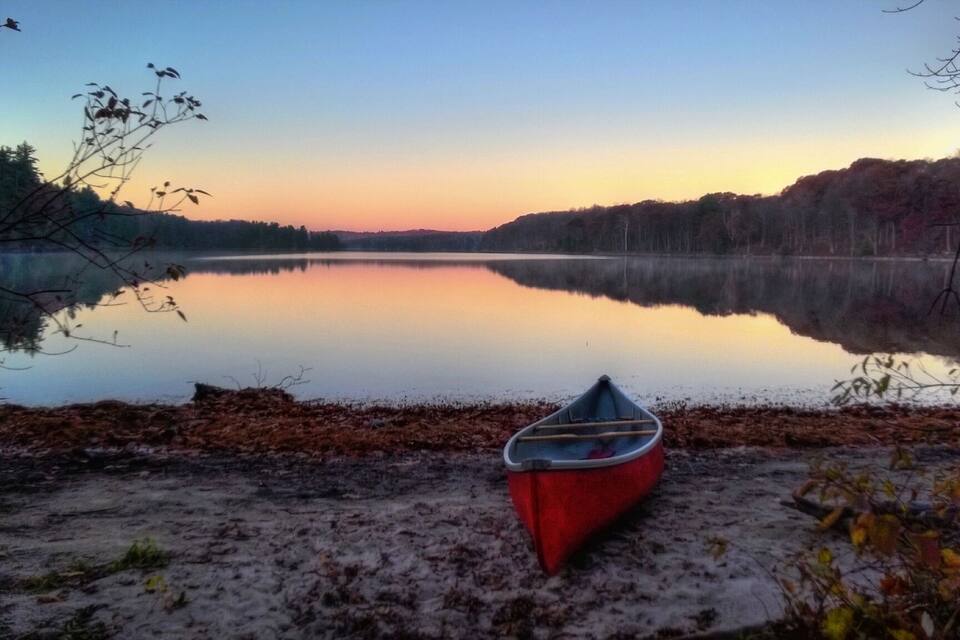 A calm lake at sunset with a canoe on the shore.