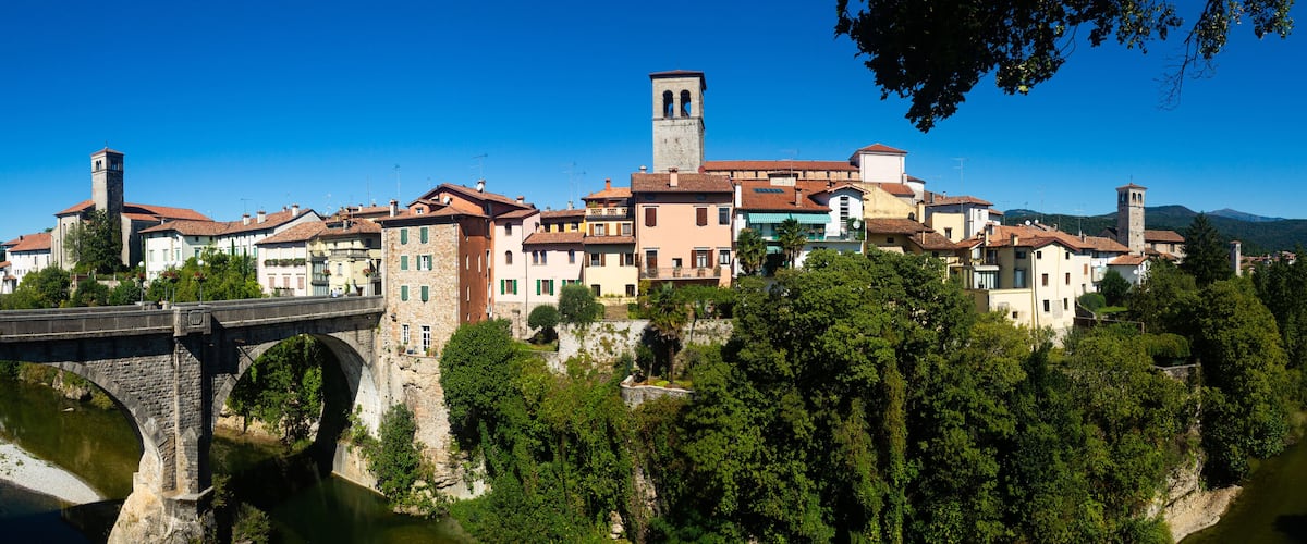 A historic town with a stone bridge over a river, surrounded by lush greenery and traditional buildings.