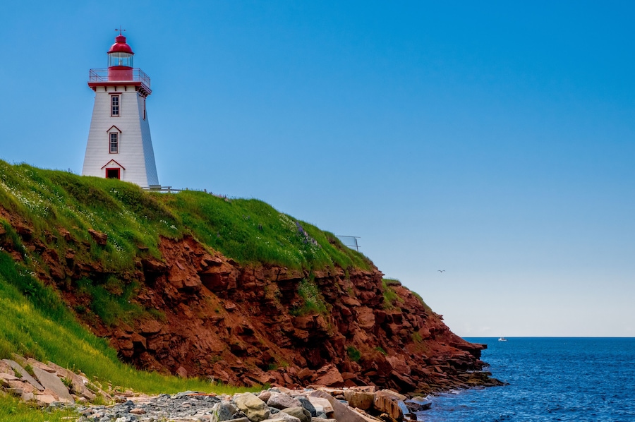 A lighthouse on a grassy cliff by the sea.