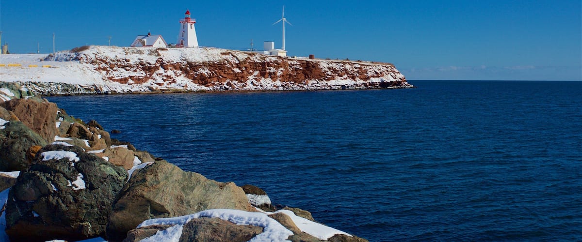 A lighthouse, a wind turbine, and a rocky shoreline with snow.