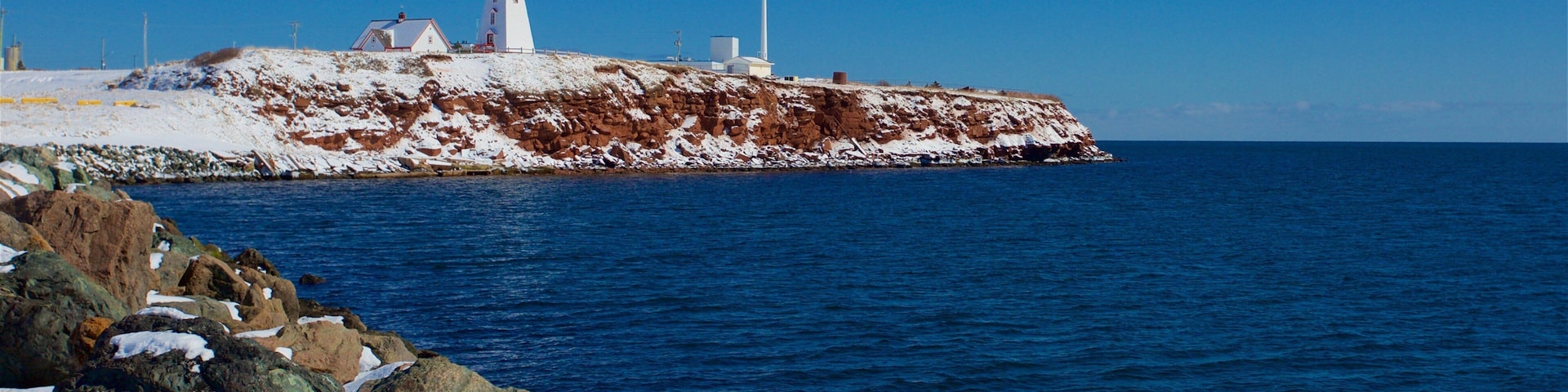 A lighthouse, a wind turbine, and a rocky shoreline with snow.