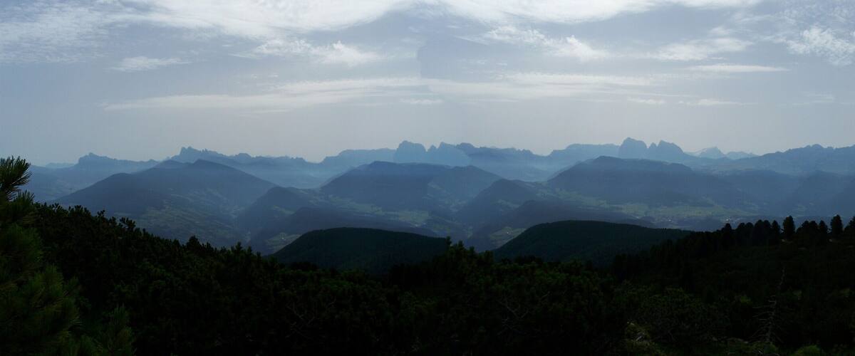 A mountainous landscape with dense forests and a range of peaks under a cloudy sky.