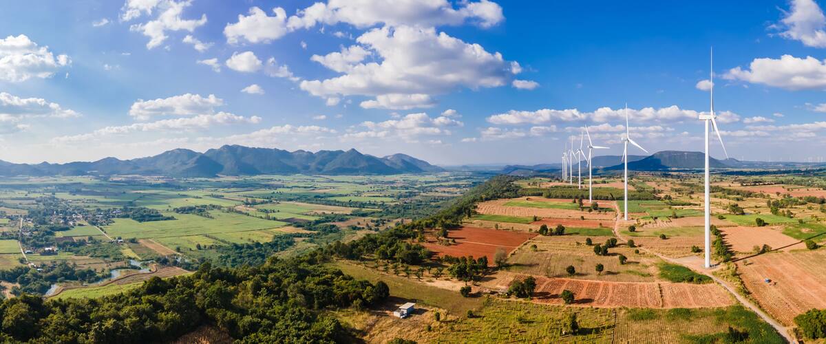 A landscape with wind turbines, green fields, and mountains in the background.