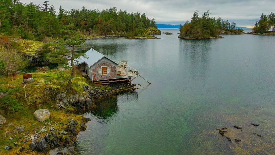 A remote wooden house on stilts by a calm lake surrounded by dense forest.