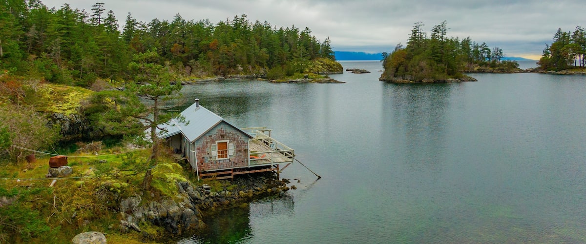 A remote wooden house on stilts by a calm lake surrounded by dense forest.