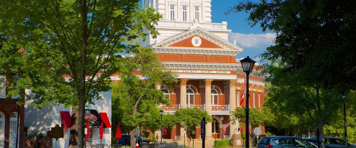 A courthouse with a clock tower, surrounded by trees and a street with parked cars.