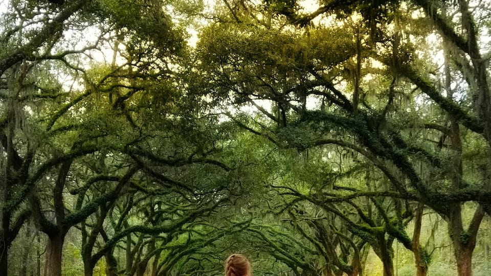 Una mujer caminando por un camino bordeado de árboles.
