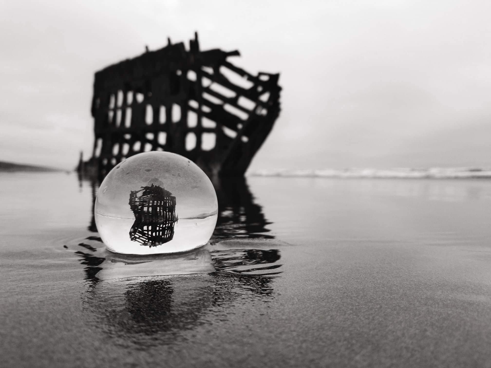 A glass bubble on a wet surface with a reflection of a pier structure.