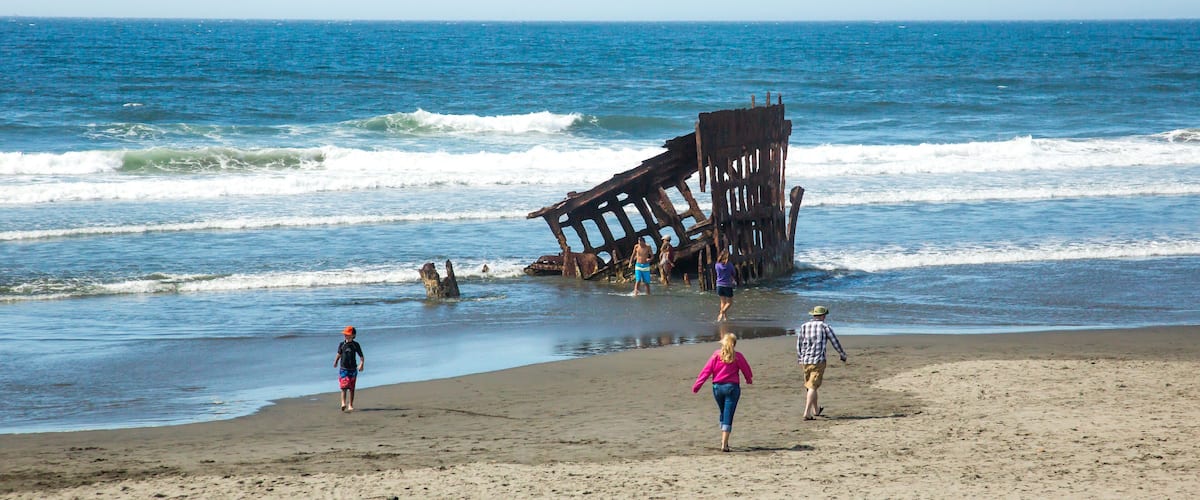 A beach with a large, rusted shipwreck in the water.