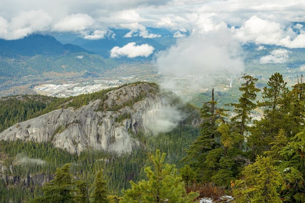 Un paysage montagneux caractérisé par de vastes forêts, des affleurements rocheux et une vue lointaine sur une ville.