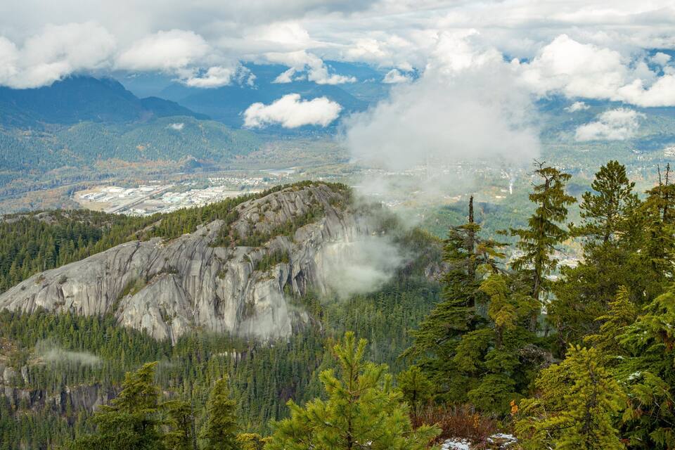 Un paisaje montañoso con bosques densos, afloramientos rocosos y una vista distante de un pueblo.