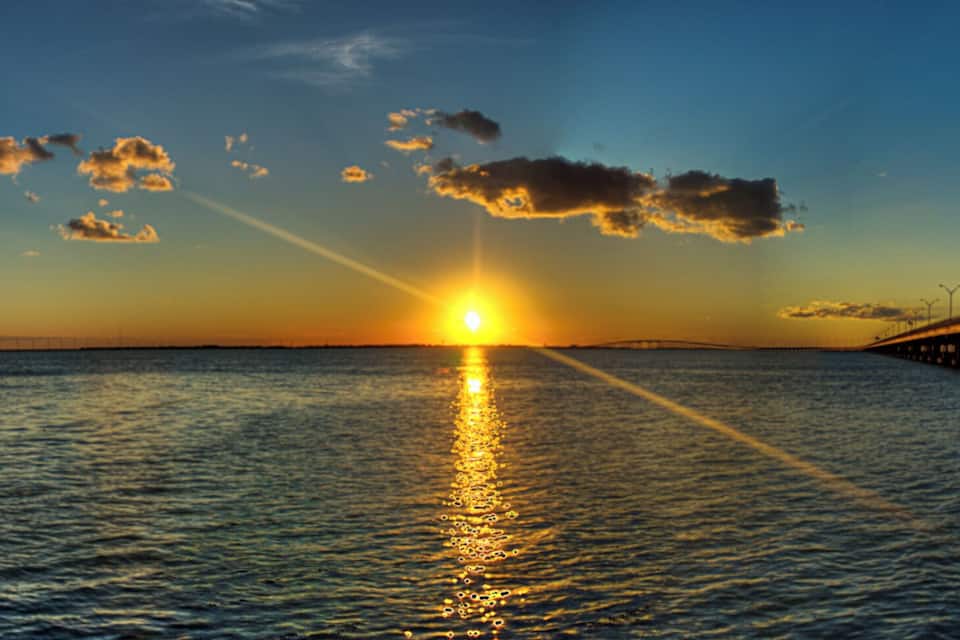 Un coucher de soleil sur une étendue d’eau, avec un pont qui s’étend vers l’horizon.