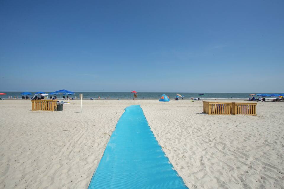 Una platja amb un estel blau que condueix a l'aigua, barreres de fusta i sombrerelles de platja.