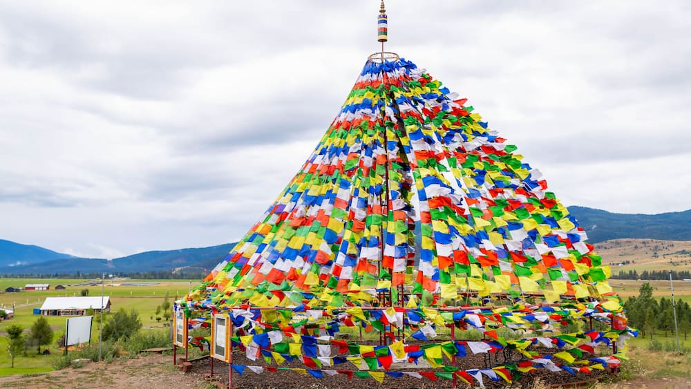 A colorful prayer flag installation in a rural landscape with mountains in the background.