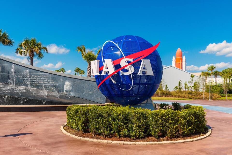 Logotipo da NASA de uma nave espacial, um foguete e um edifício com palmeiras ao fundo.