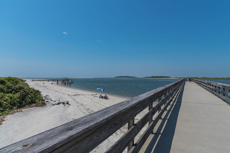 A wooden boardwalk leading to a sandy beach with a clear blue sky and calm sea.