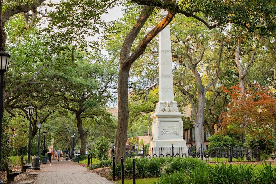 A park with a tall monument, trees, and a paved walkway.