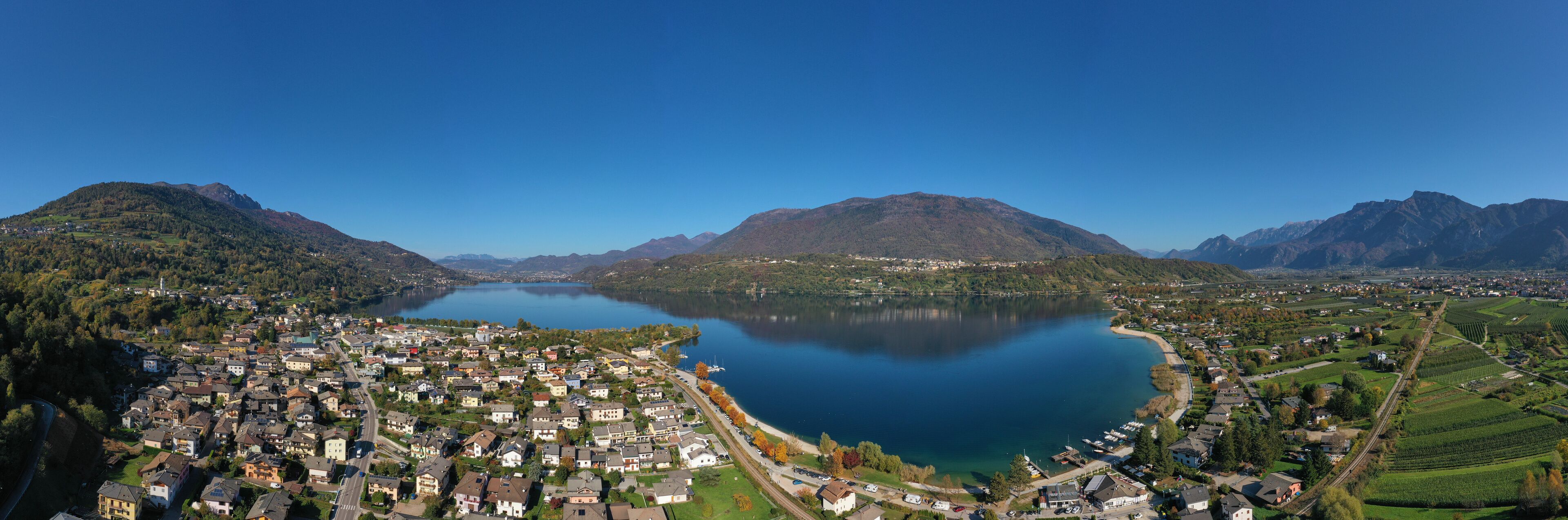 Aerial view of Lake Caldonazzo north of Italy. In the background the trees, Alps, blue sky. Reflection of mountains in water. Autumn season. Multi-colored palette of colors