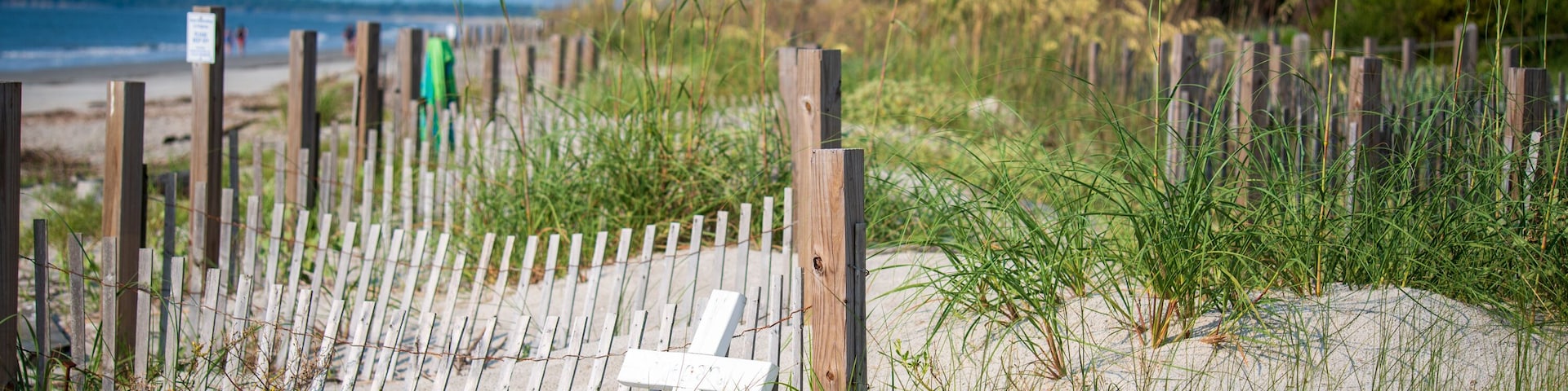 A sandy beach with a wooden fence and a white cross.