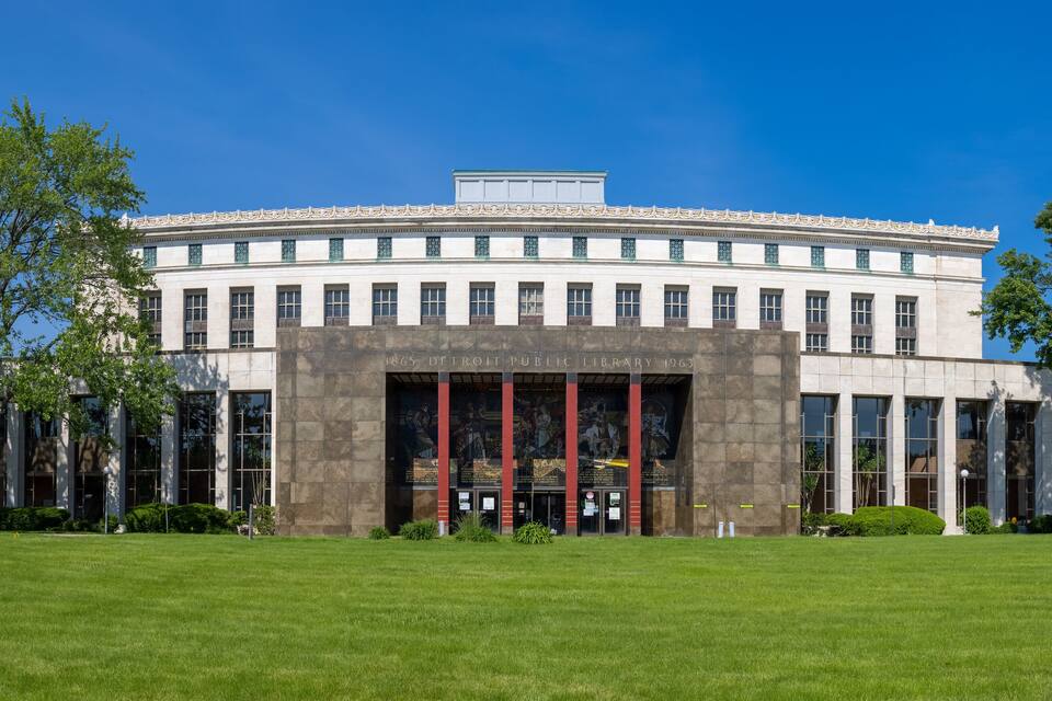 Een groot, historisch gebouw met een centrale ingang, omringd door een verzorgd gazon en bomen.
