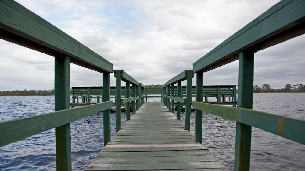 Eine hölzerne Pier, die sich über ein Gewässer erstreckt, mit einem bewölkten Himmel darüber.