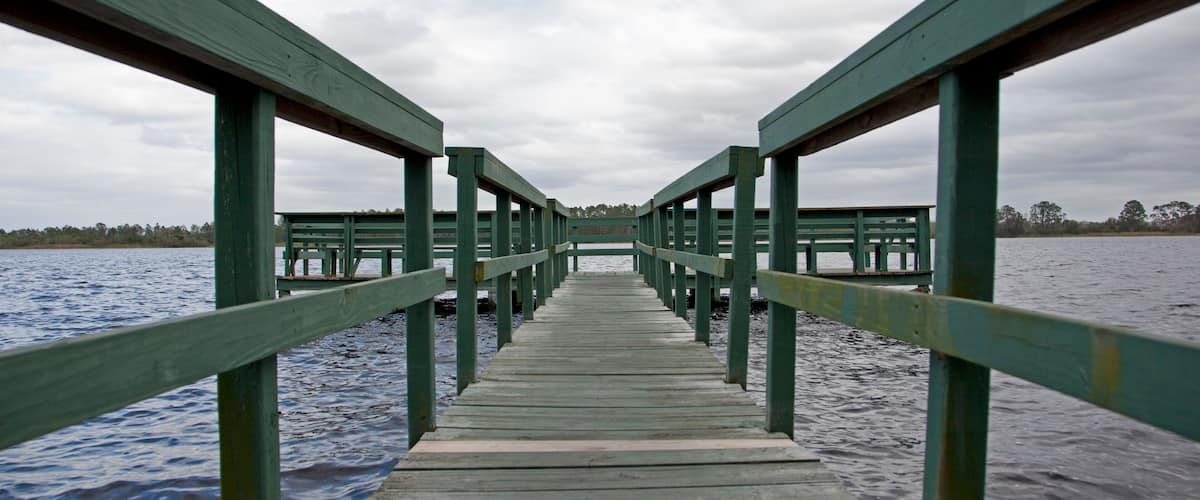 A wooden pier extending into a body of water with a cloudy sky above.