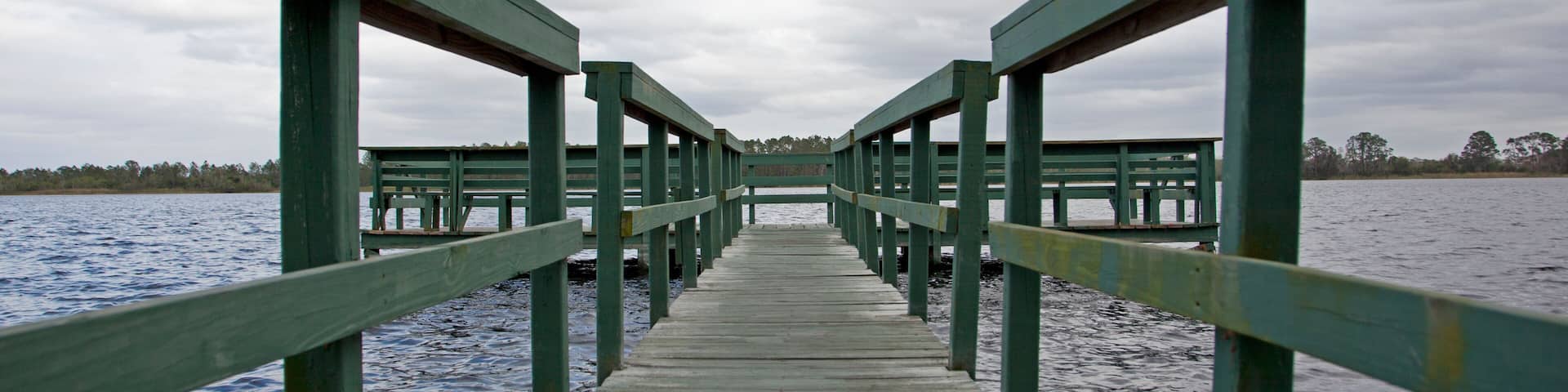 A wooden pier extending into a body of water with a cloudy sky above.