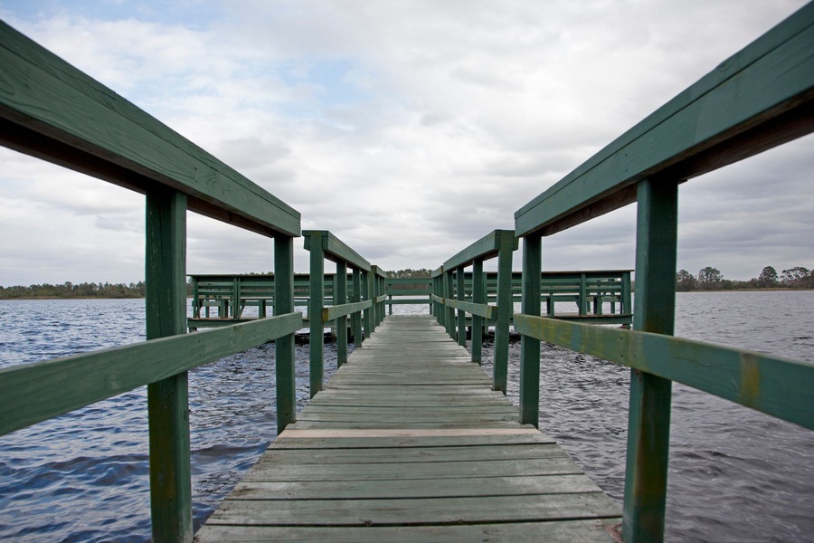 A wooden pier extending into a body of water with a cloudy sky above.