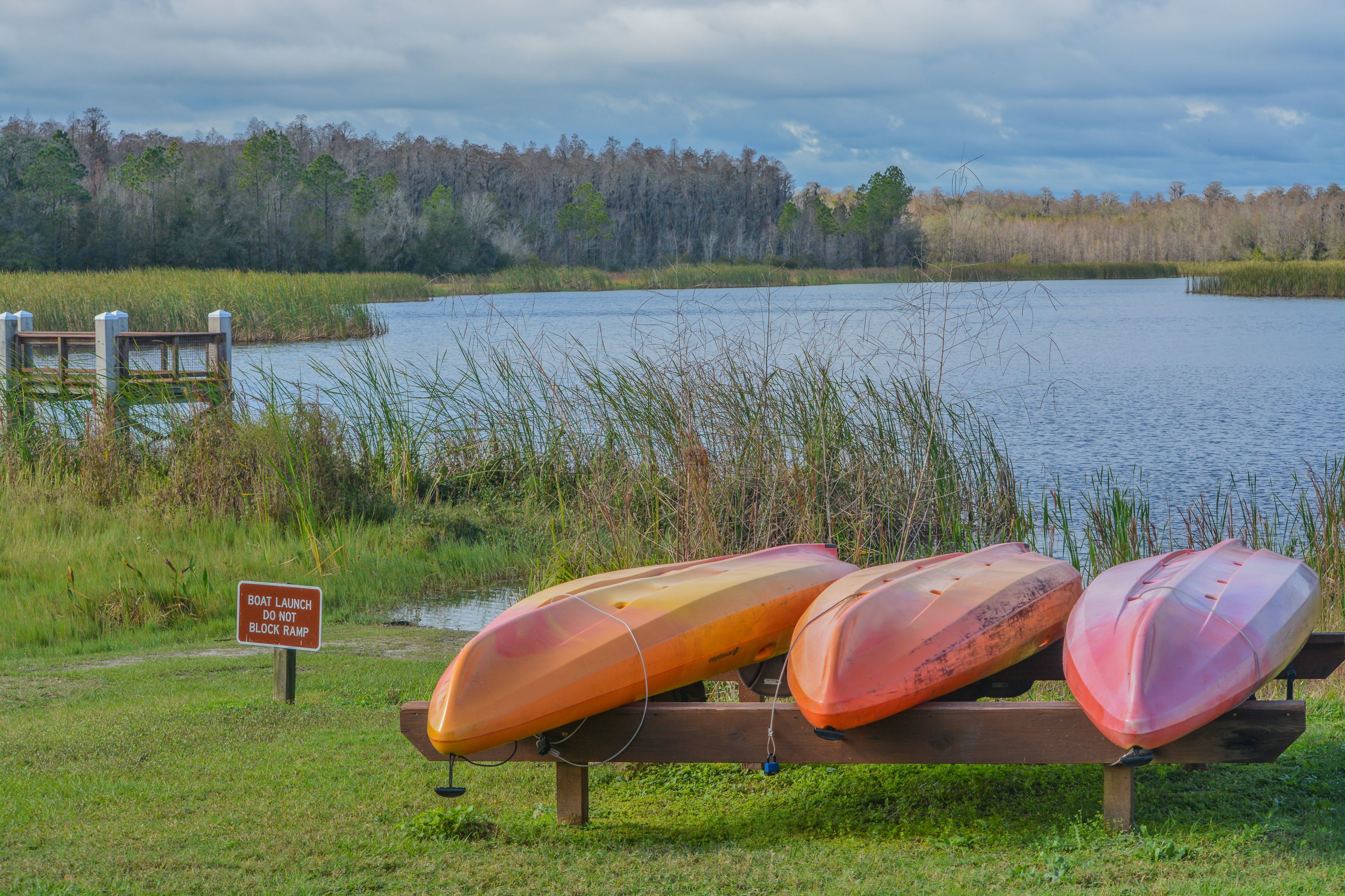 A lake with three canoes on a dock, surrounded by grassy areas and trees.