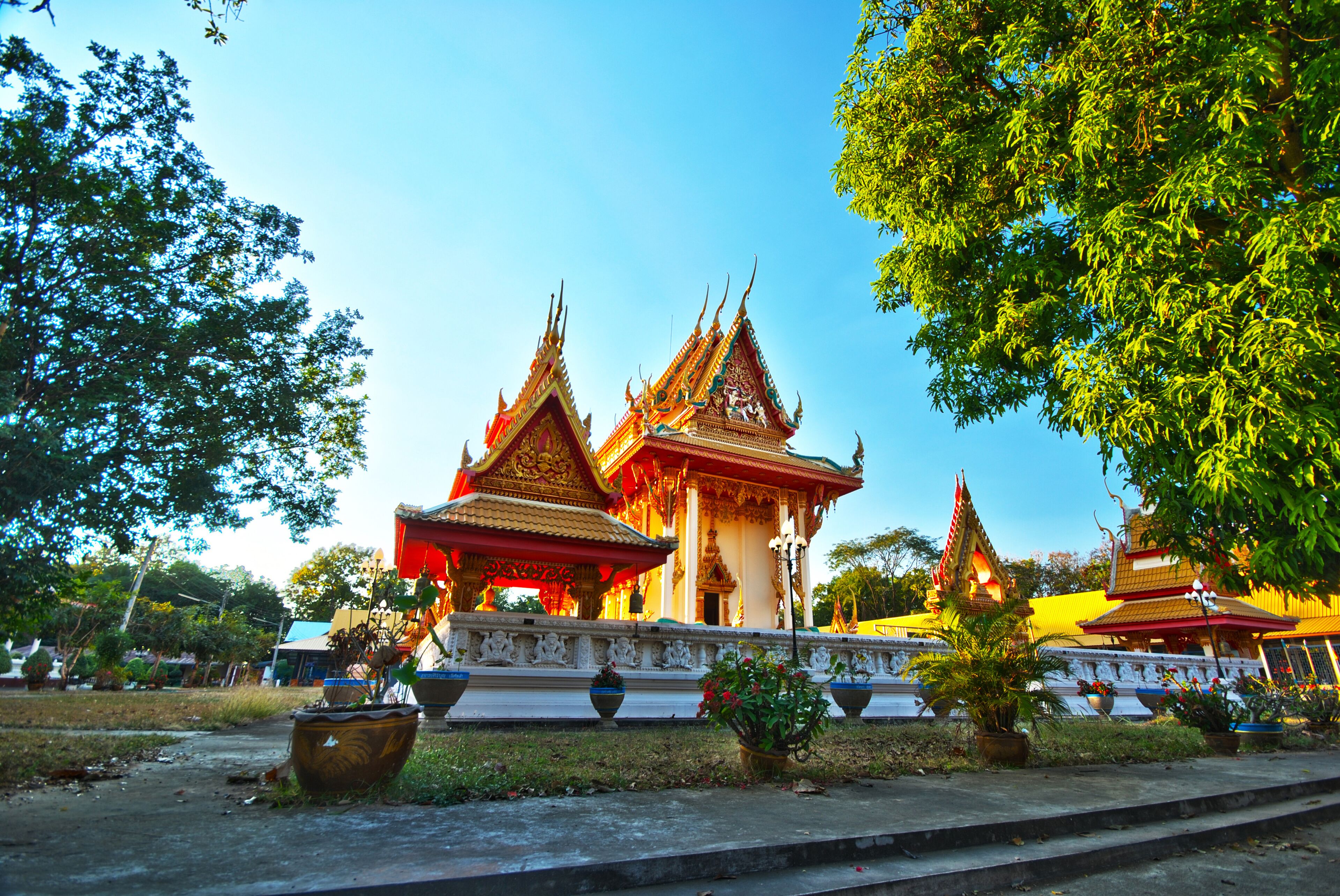 A traditional Thai temple with ornate architecture and a well-maintained garden.
