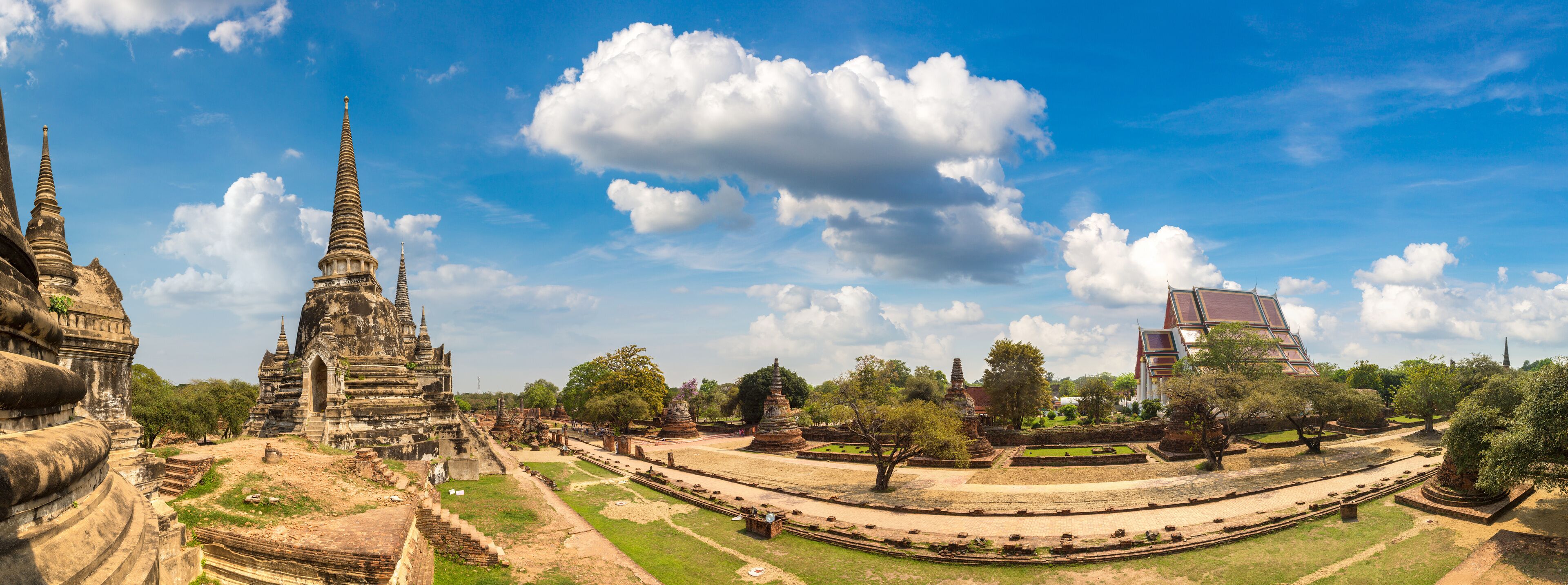 Ancient temple ruins with tiered structures and a modern building in the background.