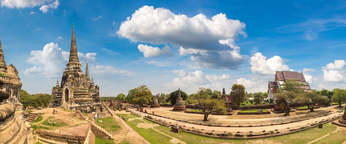 Ancient temple ruins with tiered structures and a modern building in the background.
