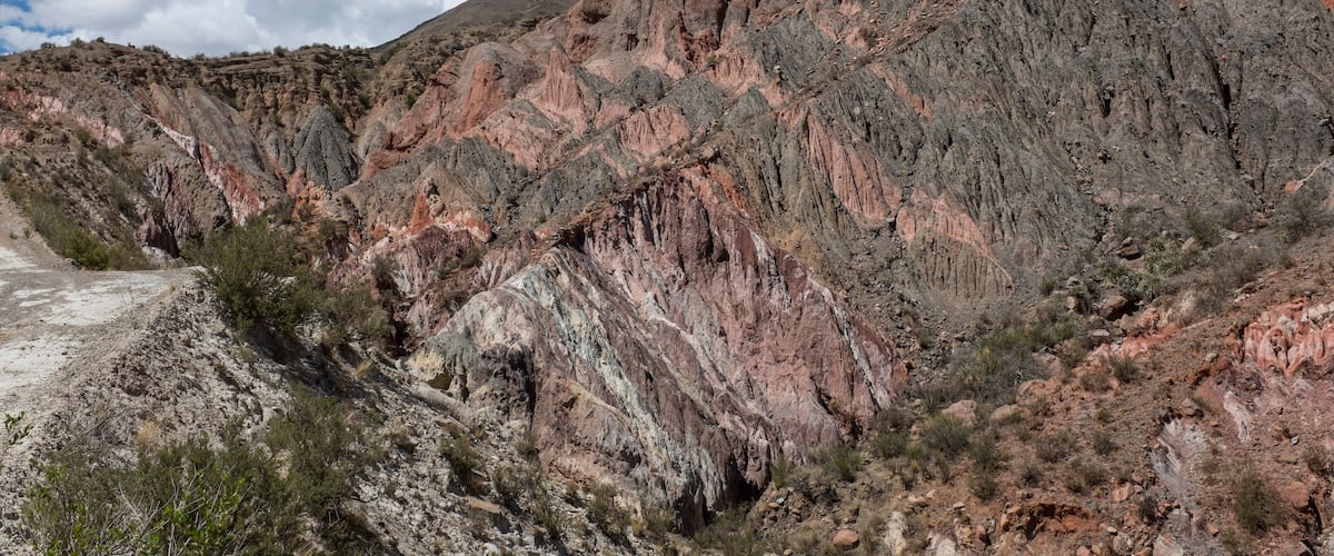 A rugged mountain landscape with reddish-brown rock formations and sparse vegetation.