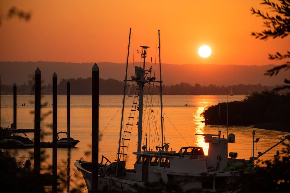 A sunset over a calm river with boats docked at the pier.