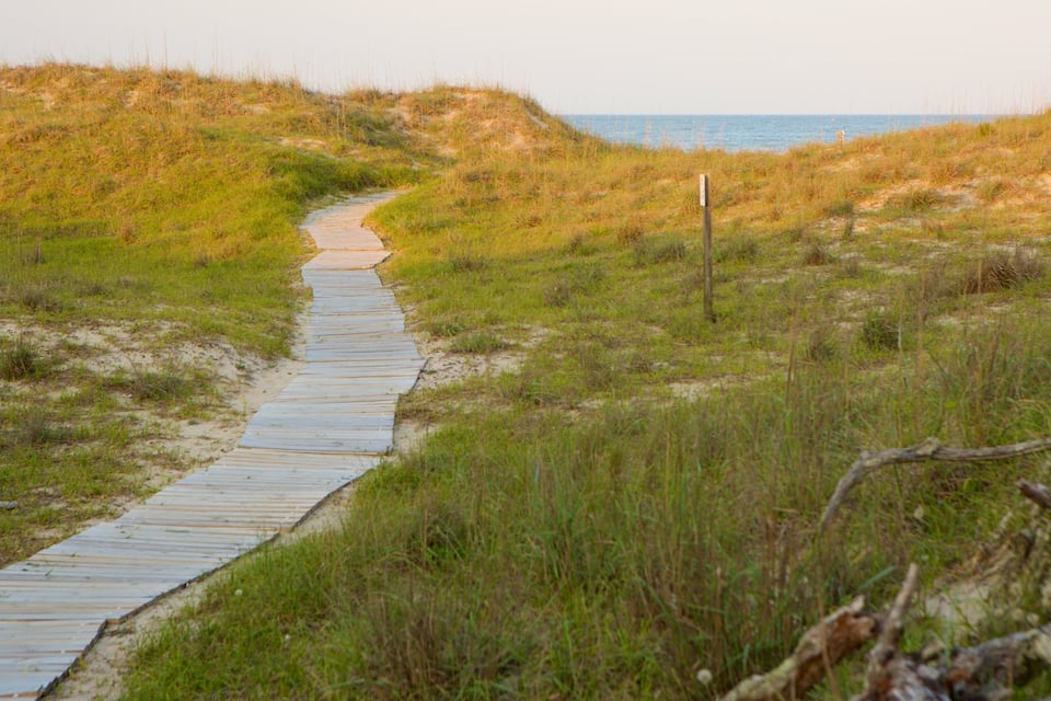 A wooden boardwalk leading to the beach, surrounded by grassy dunes.