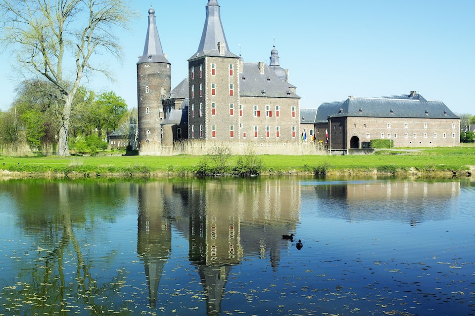 A historic castle with two towers, a moat, and a reflection in the water.