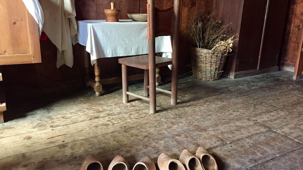 A rustic interior with wooden floors, a table with a white cloth, a chair, and a basket of dried plants.