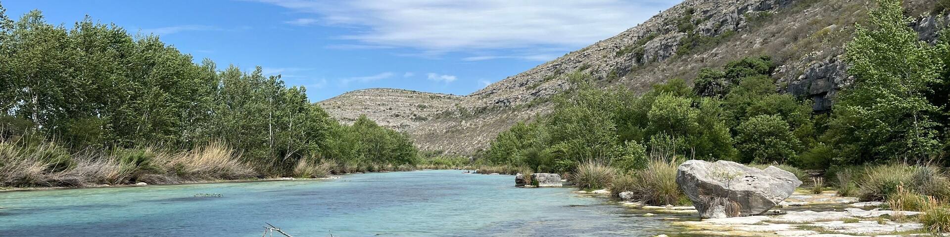 Un río claro con riberas rocosas y vegetación verde.