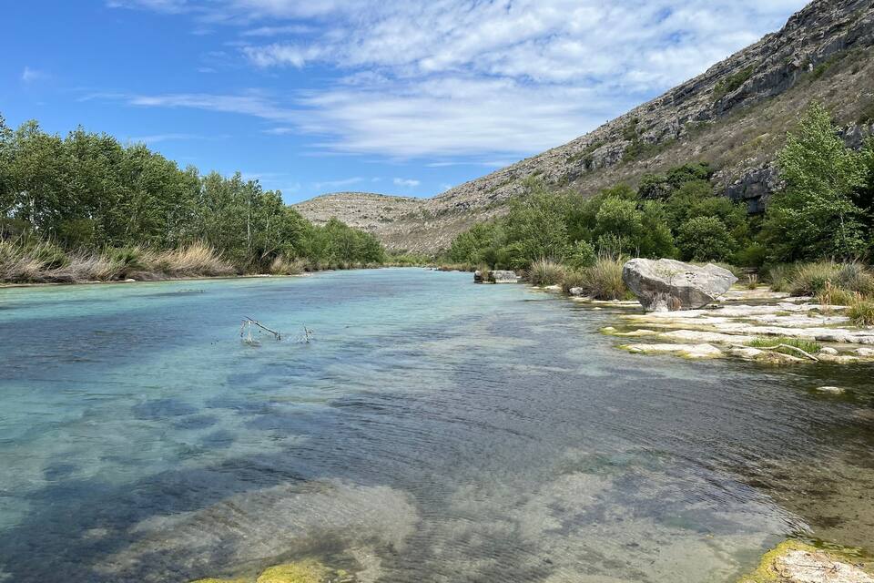 Un río claro con riberas rocosas y vegetación verde.