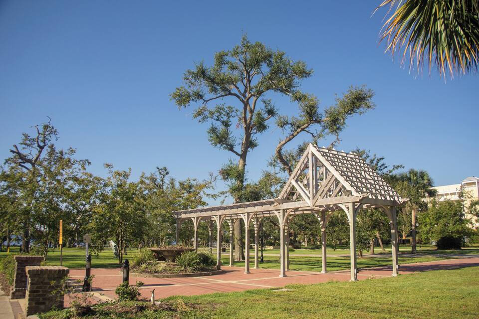A gazebo in a park with a large tree and a building in the background.