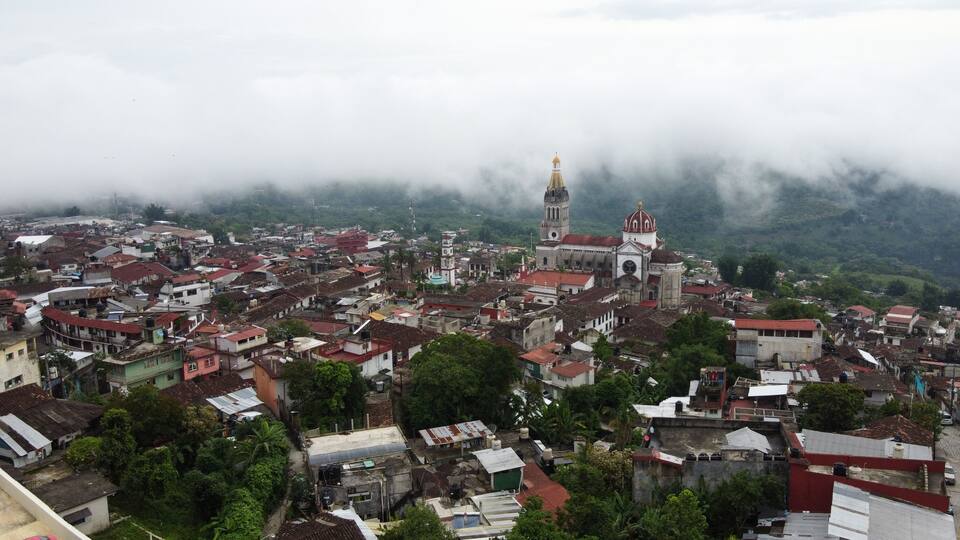 A town with a prominent church featuring a bell tower and dome, surrounded by dense residential buildings and lush greenery.