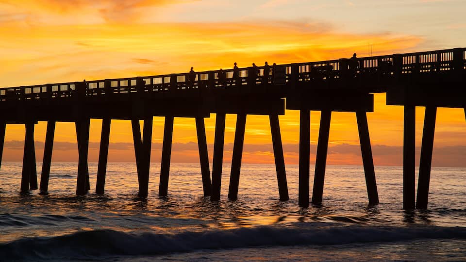 A pier extending into the ocean at sunset with a vibrant sky.