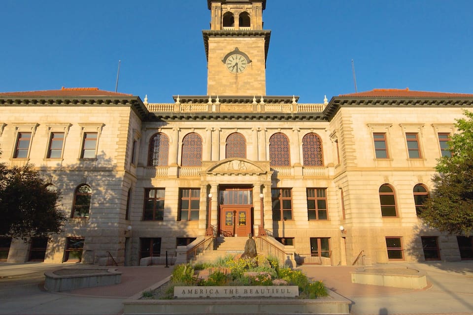 A historic building with a clock tower, arched windows, and a statue in front.
