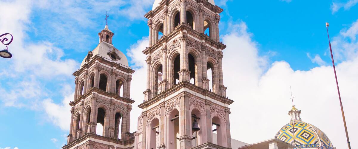A historic church with two bell towers and a colorful sign in front.