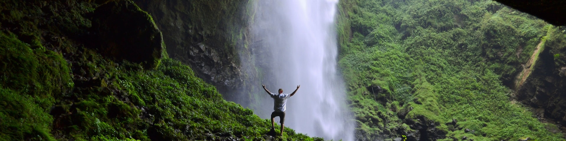 A waterfall cascading through a cave opening, surrounded by lush green vegetation.