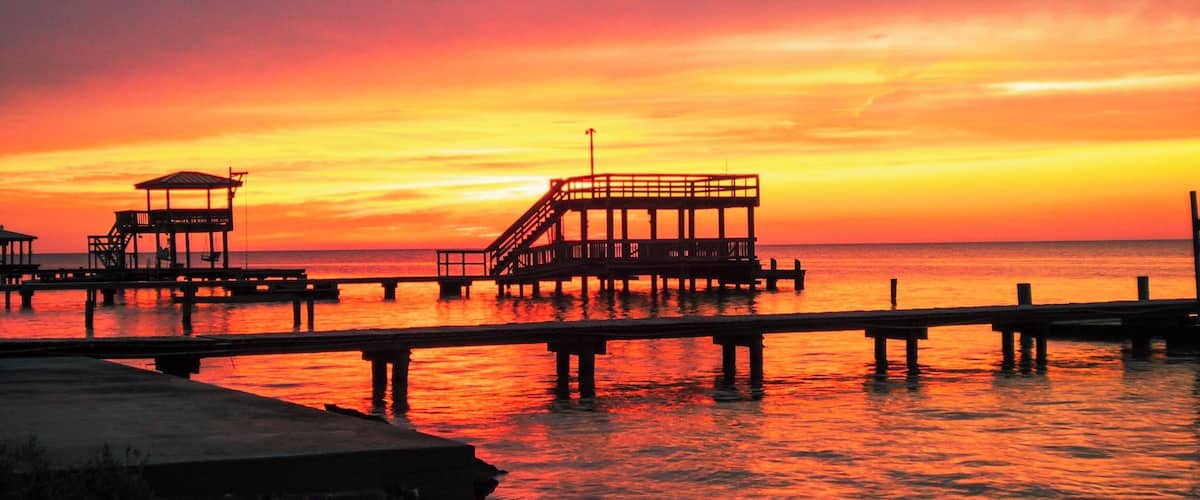 A sunset over a pier with a wooden structure and rocky shoreline.